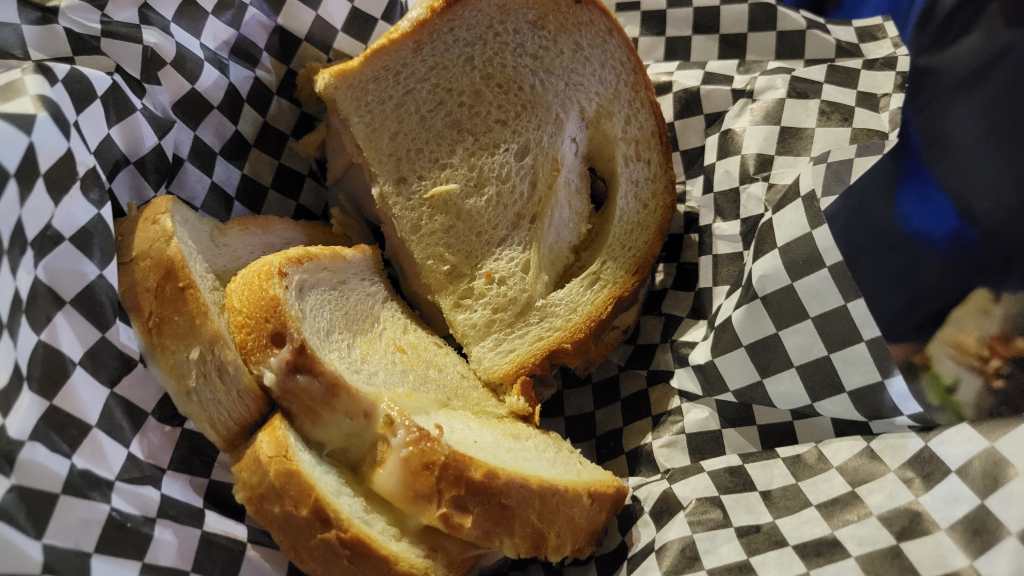 A basket lined with black and white checkered paper containing slices of a sandwich, showcasing soft bread with a light golden crust.