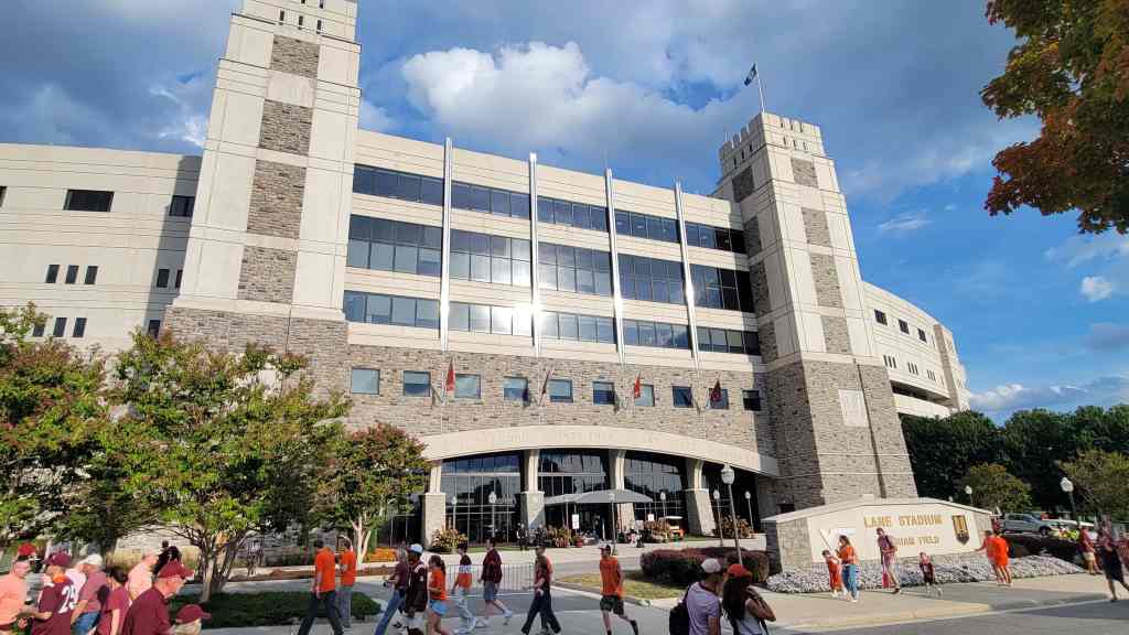 Exterior view of Lane Stadium with a crowd of fans walking towards the entrance on a sunny day.