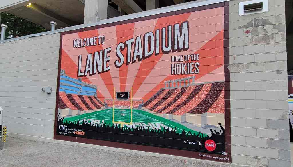 A mural welcoming visitors to Lane Stadium, home of the Hokies, featuring a vibrant design with a football field and cheering fans in the foreground.