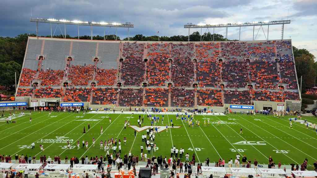 A college football stadium filled with fans in orange and maroon colors, showcasing teams warming up on the field during a game.